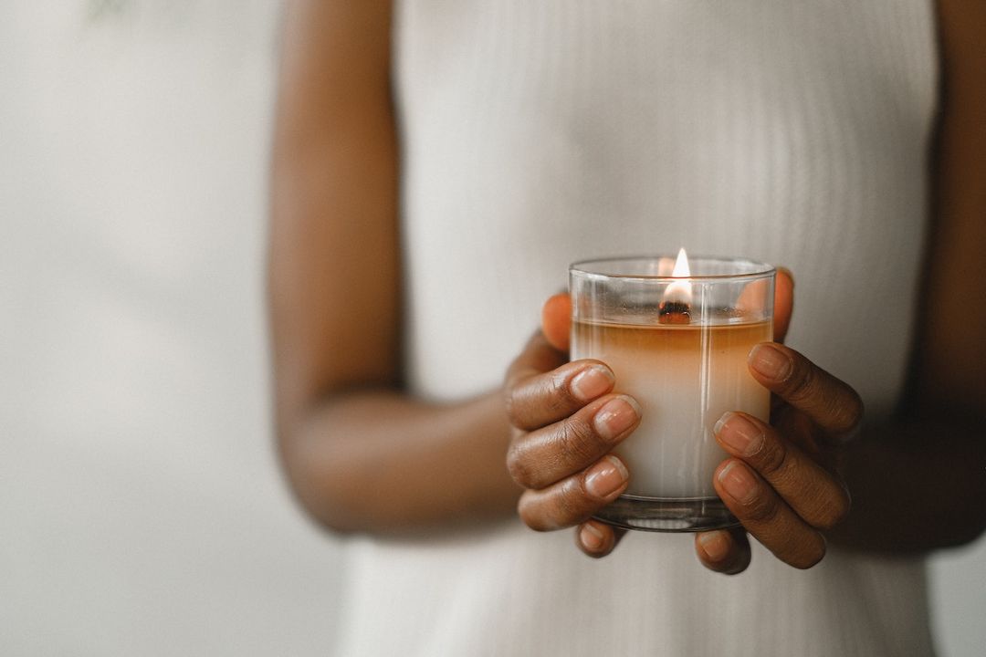 Woman holding a lit candle with both of her hands.